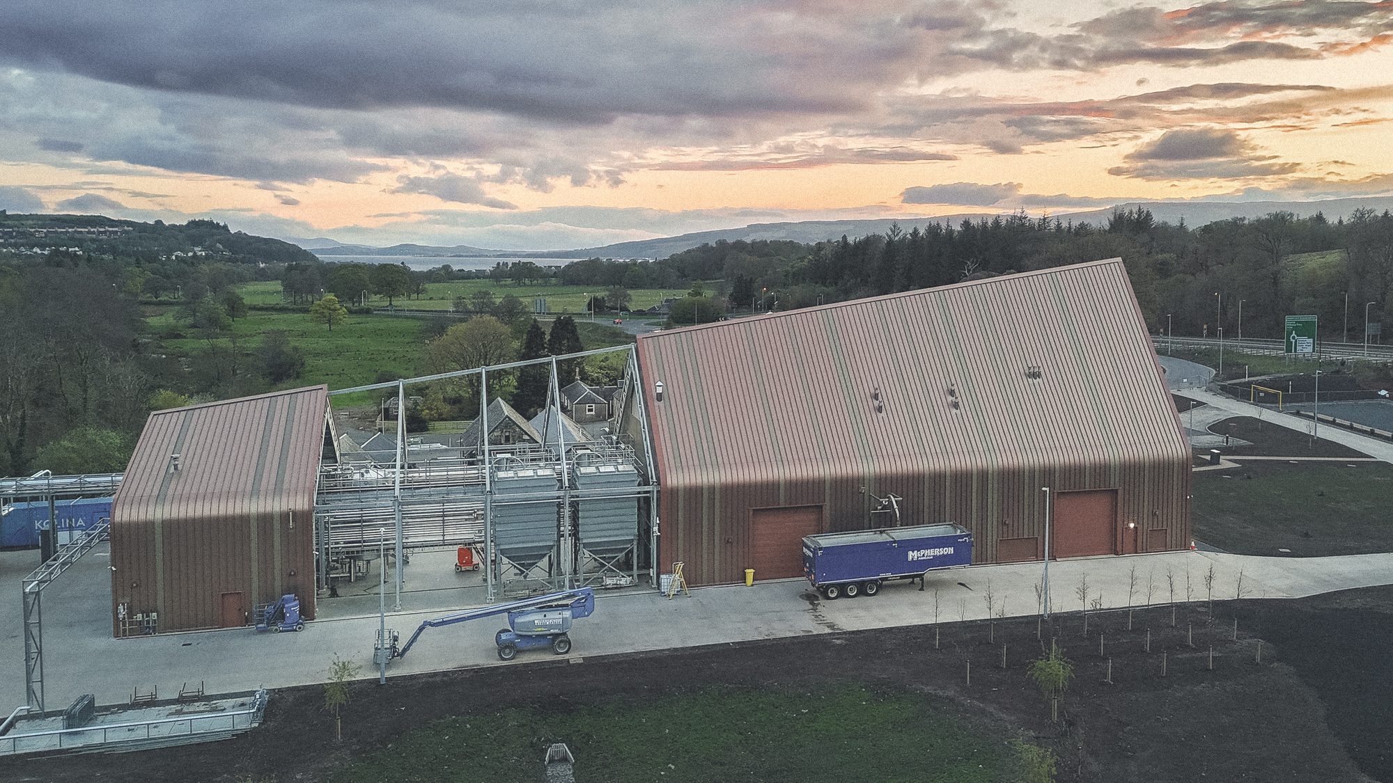Ardgowan Distillery, Inverkip — Luftbild der Gesamtanlage zur Abenddämmerung, im Hintergrund der Firth of Clyde und die Hügel von Argyll