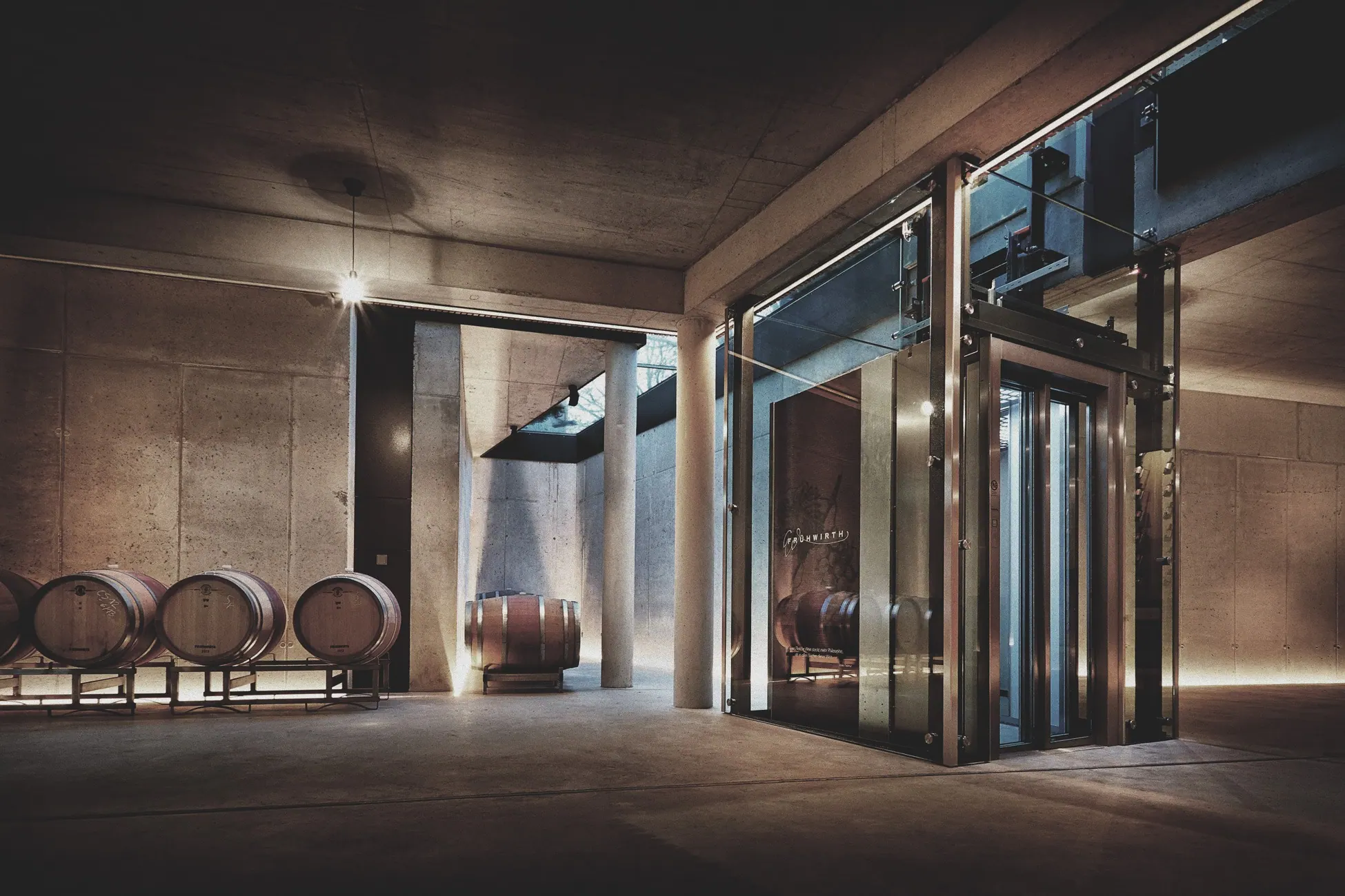 Bio-Weingut Frühwirth, Thermenregion — Holzfässer im Sichtbetonraum neben dem verglasten Eingang