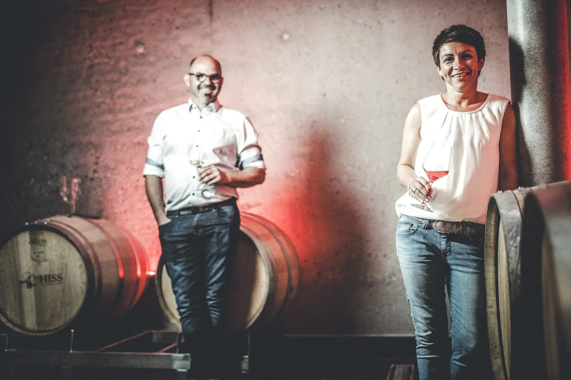 Weingut Hiss, Kaiserstuhl — Winzerpaar mit Gläsern zwischen Holzfässern