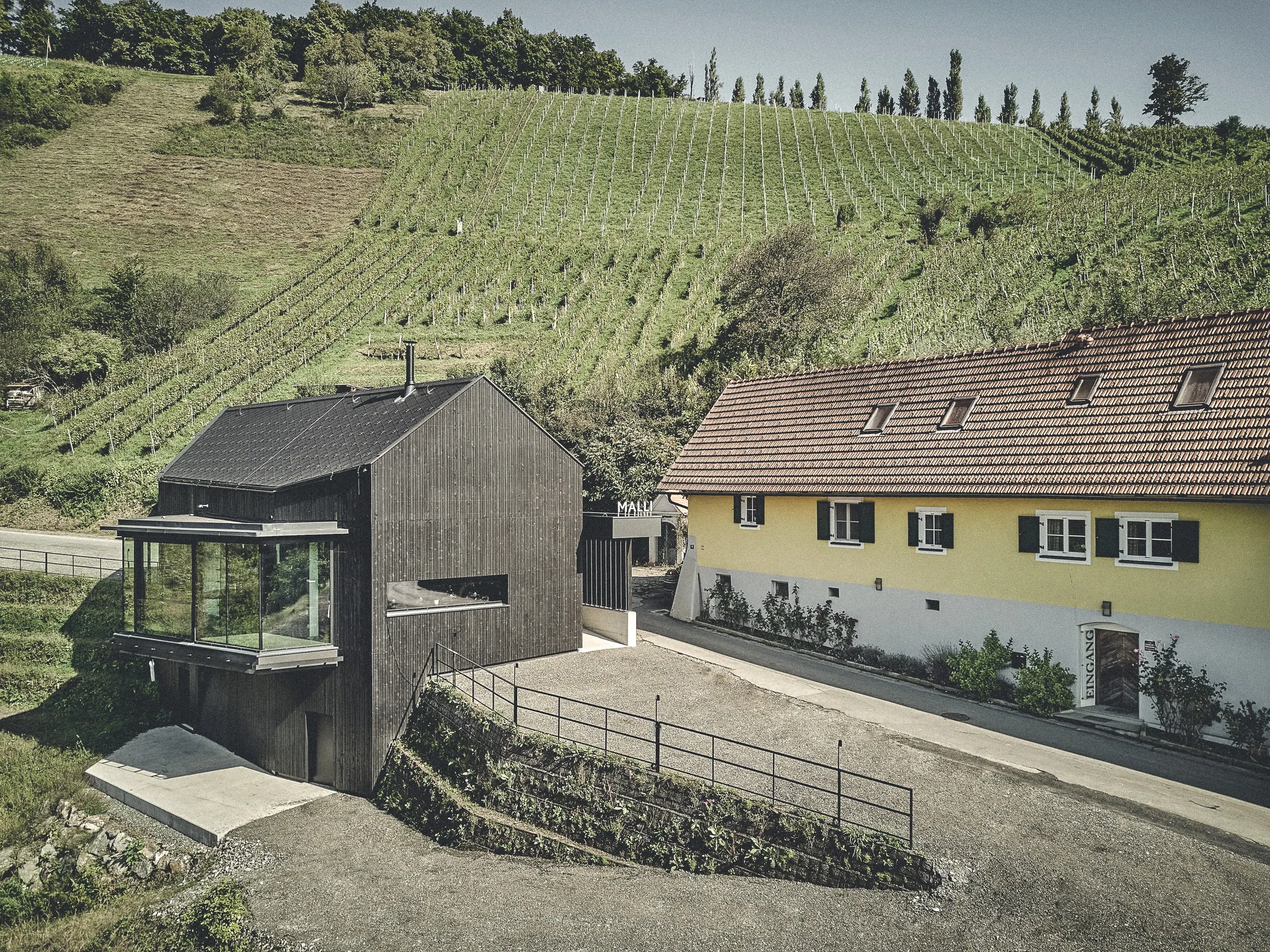 Weingut Malli, Südsteiermark — Neubau mit Glasvorbau neben dem alten Wohnhaus, dahinter die Reben