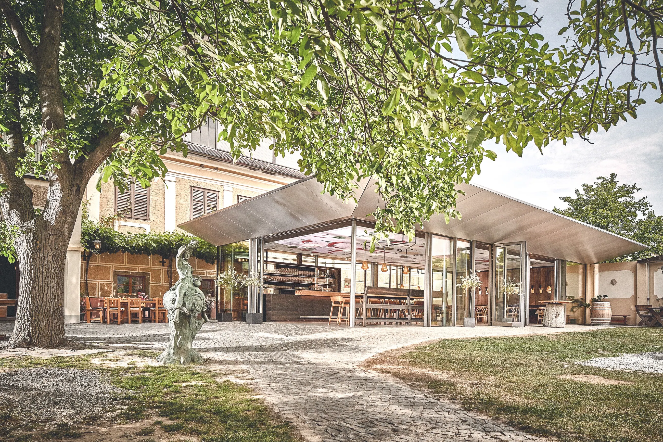 Weingut Mang, Wachau — Gastgarten unter alten Bäumen vor dem geöffneten Glaspavillon
