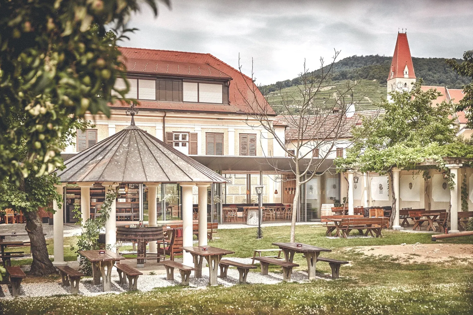 Weingut Mang, Wachau — Hof mit Pavillon und Bänken, dahinter Kirchturm und Weinberge