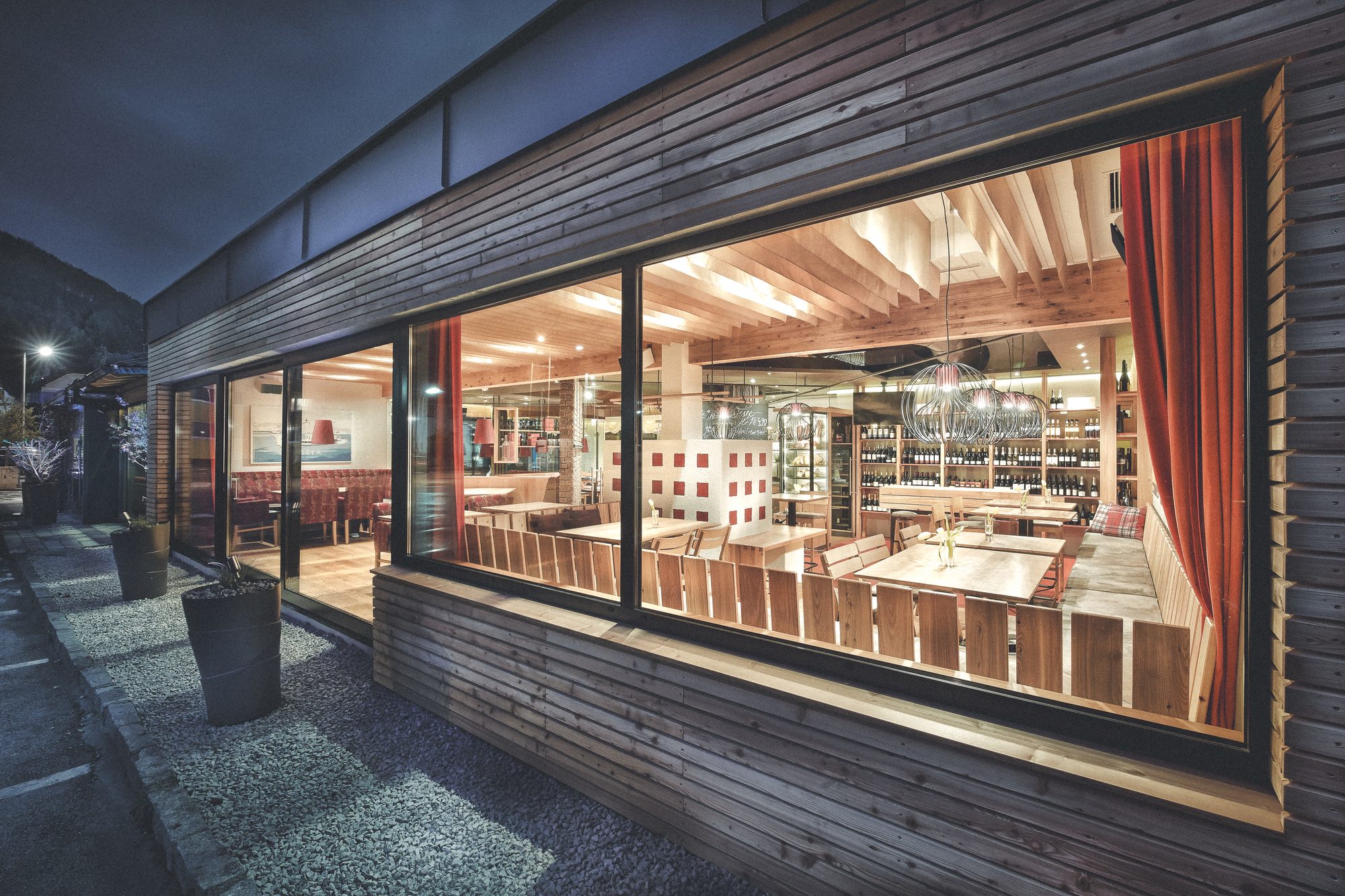 Restaurant Steiner, Pinsdorf — Lärchenfassade bei Nacht, das Panoramafenster gibt den Blick in den Gastraum frei