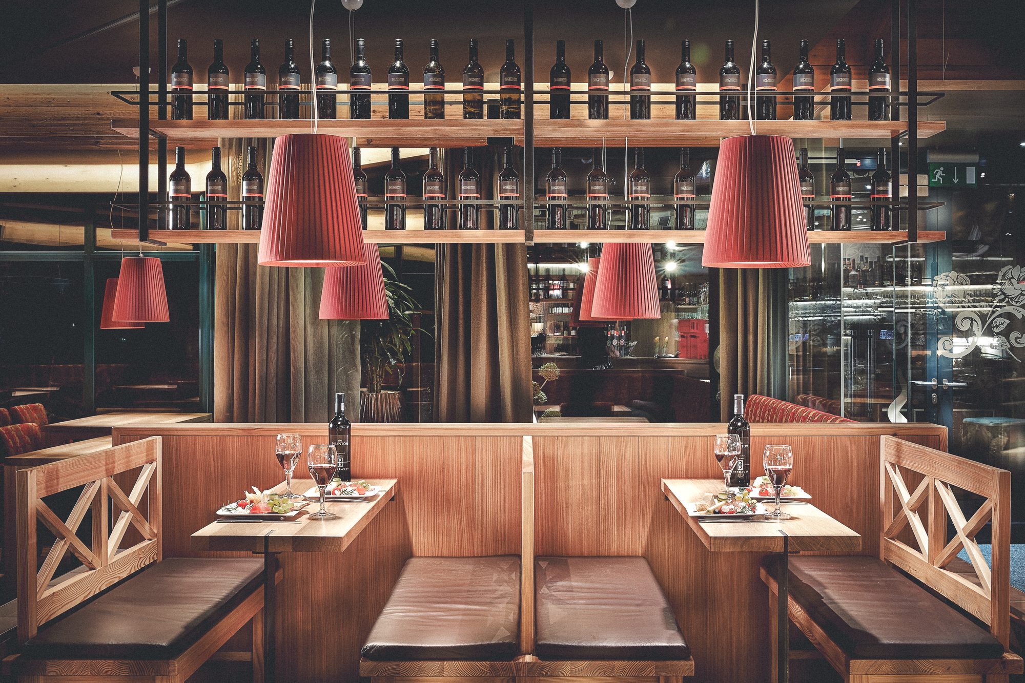 Restaurant Steiner, Pinsdorf — Holzboxen mit Lederbänken unter dem Weinflaschenregal, rote Plisseeleuchten