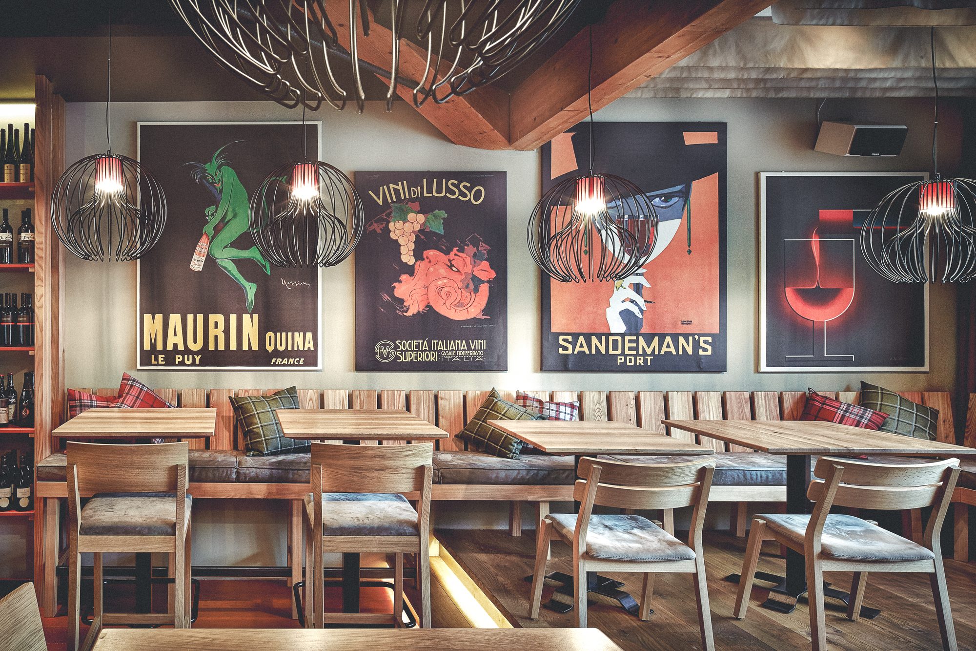 Restaurant Steiner, Pinsdorf — Sitzbank vor der Wand mit historischen Weinplakaten, darüber Käfigleuchten